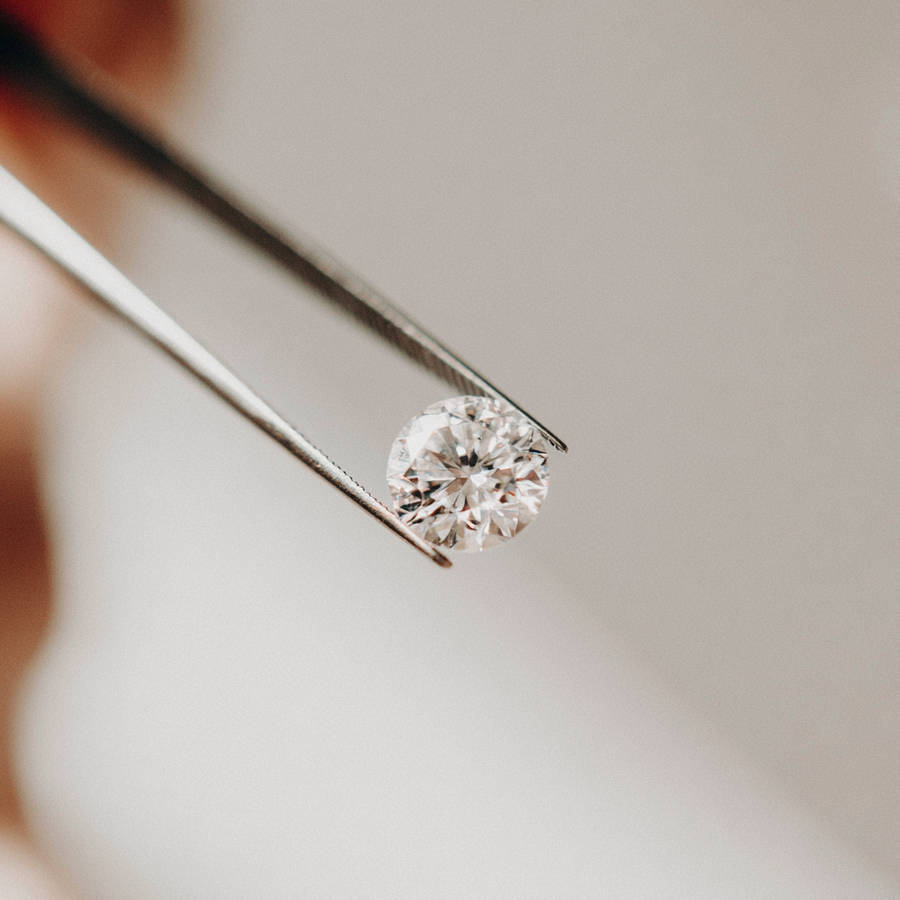 Round brilliant-cut diamond held in jeweller’s tweezers, close-up for bespoke engagement ring design and sourcing.