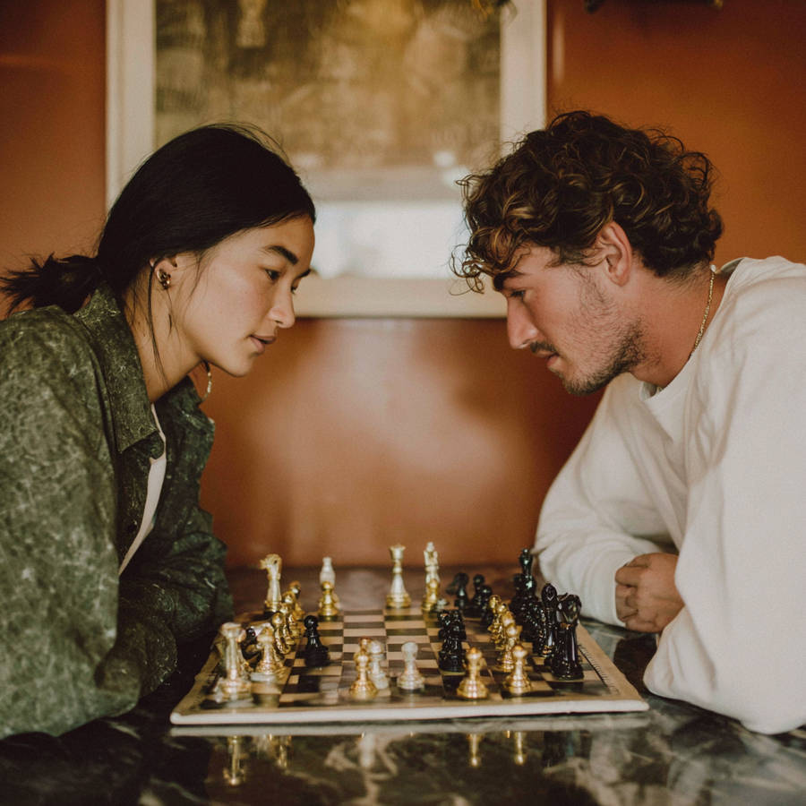 Two people lean over a chessboard at a table, focused on the next move in a cozy room.