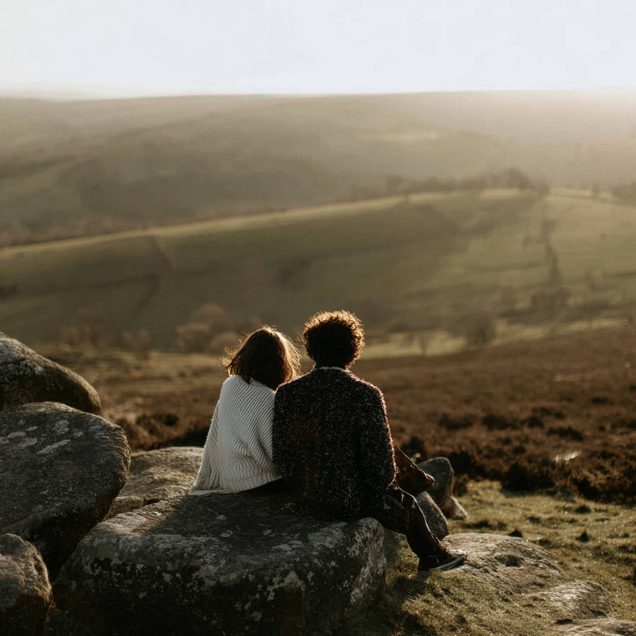 modern_couple_sitting_on_a_rock_looking_out_across_a_field