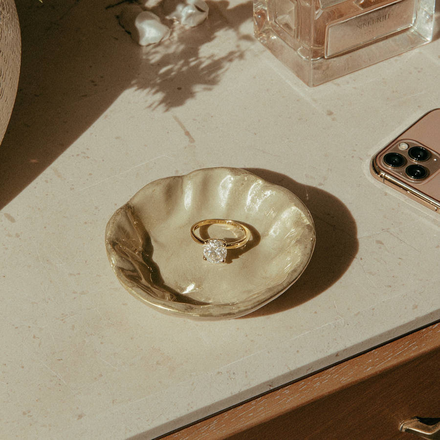 Bespoke gold engagement ring with solitaire diamond displayed in ceramic dish on dresser in warm natural light