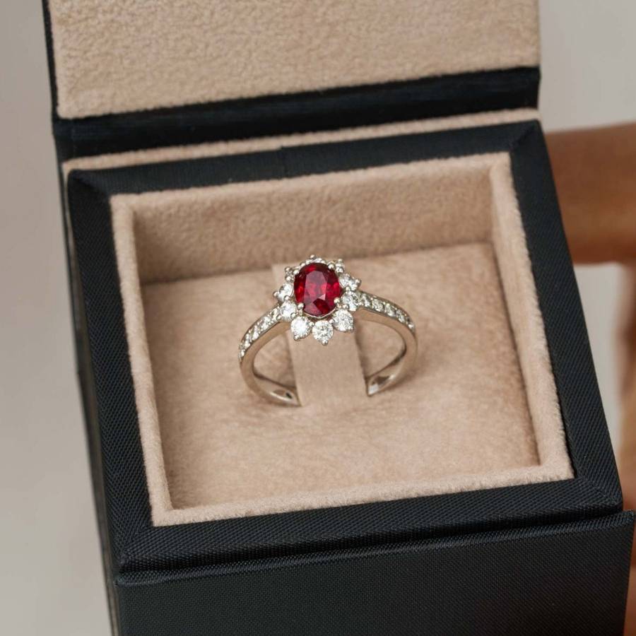 Close-up of bespoke engagement ring with red gemstone and diamond halo presented in an open ring box
