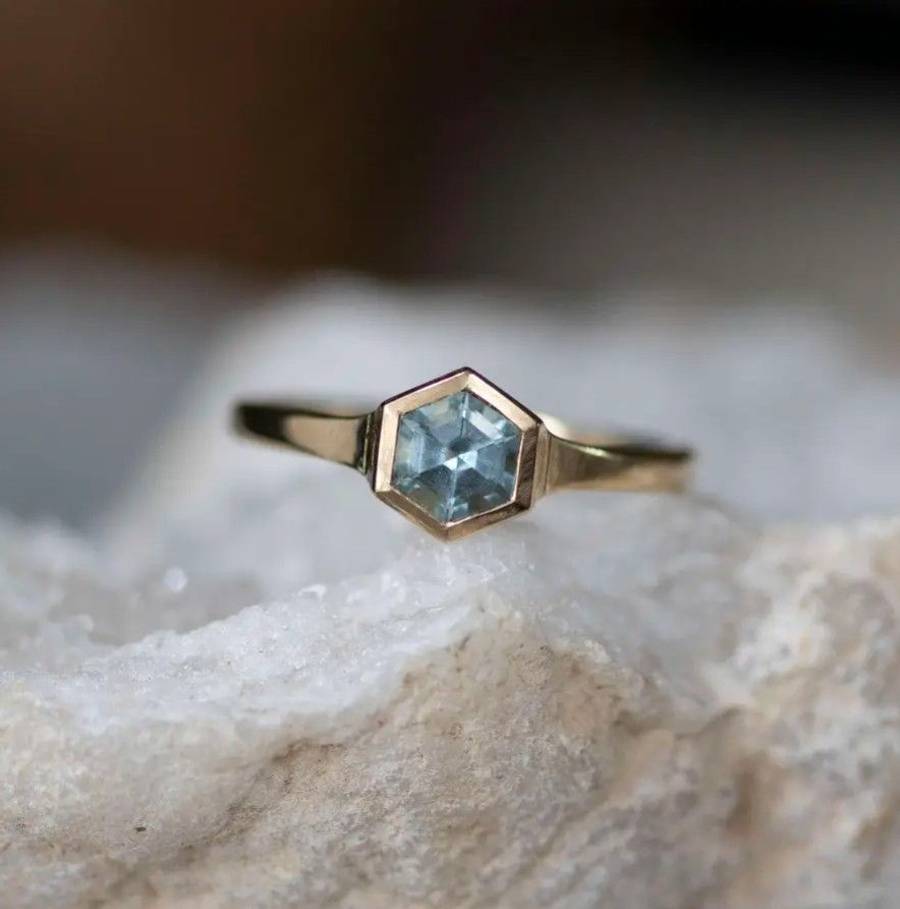 Custom hexagon-cut aquamarine ring in a bezel setting, photographed on a pale stone surface
