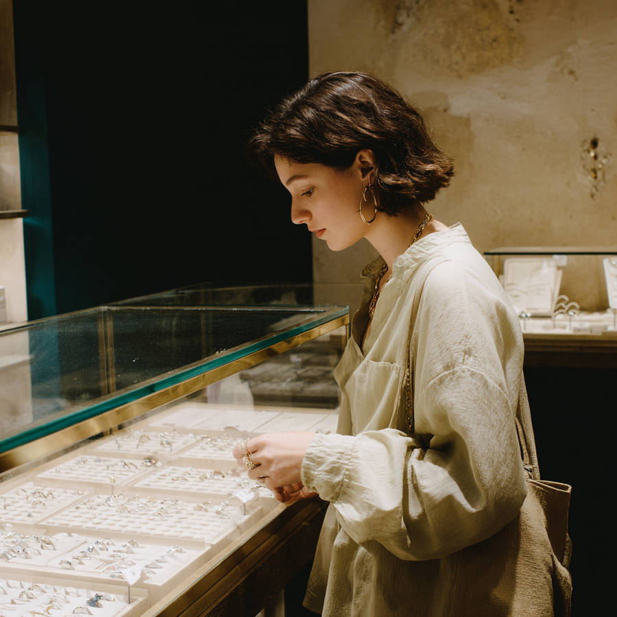 Young woman browsing bespoke engagement rings in a softly lit jewellery shop, standing beside a glass display case