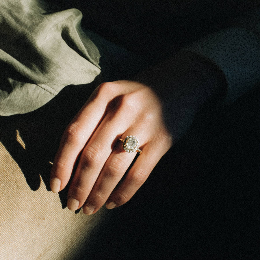 Hand wearing a bespoke halo diamond engagement ring on a gold band, lit by soft natural light.