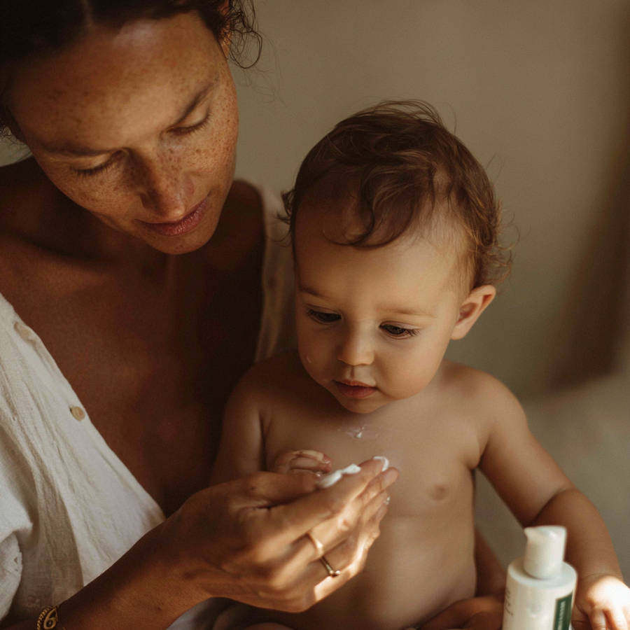 Mother applying lotion to her baby in soft natural light, wearing a bespoke engagement ring during a nurturing moment.