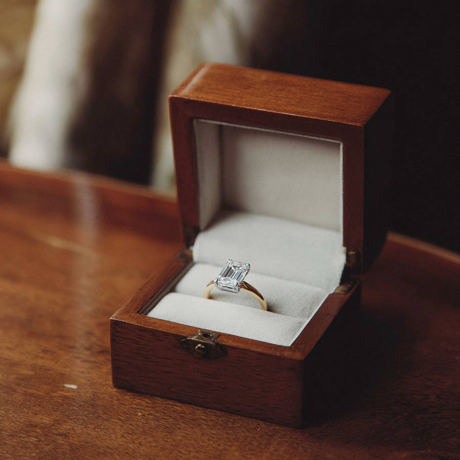 Emerald-cut bespoke engagement ring in an open wooden ring box on a table, sparkling in soft light