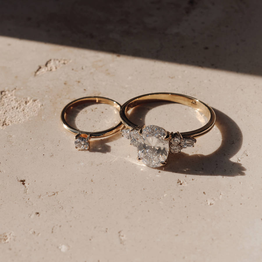 Two bespoke gold engagement rings with diamond settings resting on textured surface in warm natural light