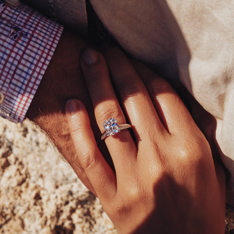 Hand wearing a custom diamond engagement ring with pavé band resting on partner’s arm in warm natural light