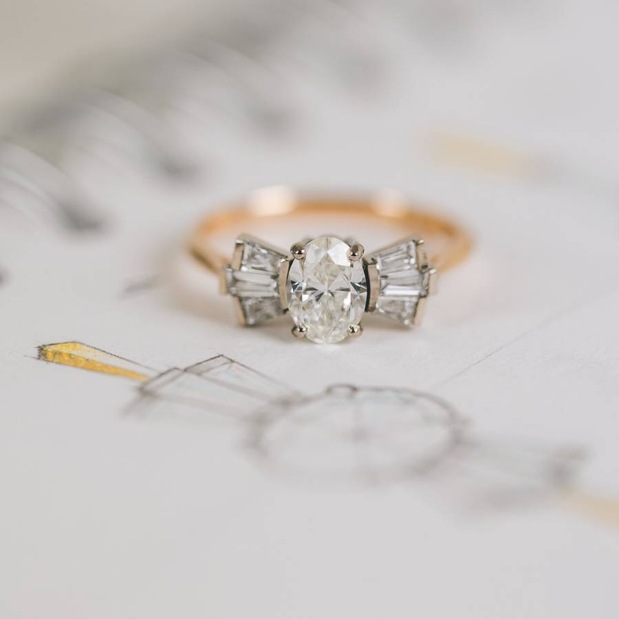 Bespoke oval diamond engagement ring with tapered baguette side stones in mixed rose and white gold, placed on design sketches