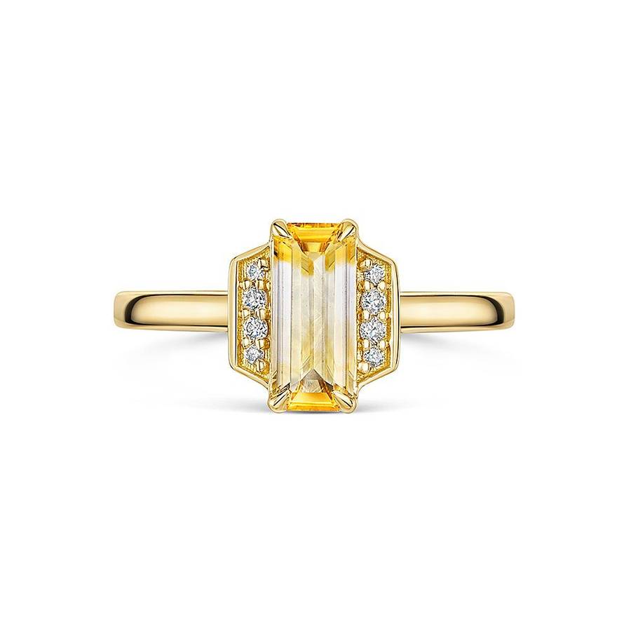 Yellow gold ring with an elongated emerald-cut yellow gemstone center, flanked by small round white diamonds in geometric side settings, displayed on a plain white background.