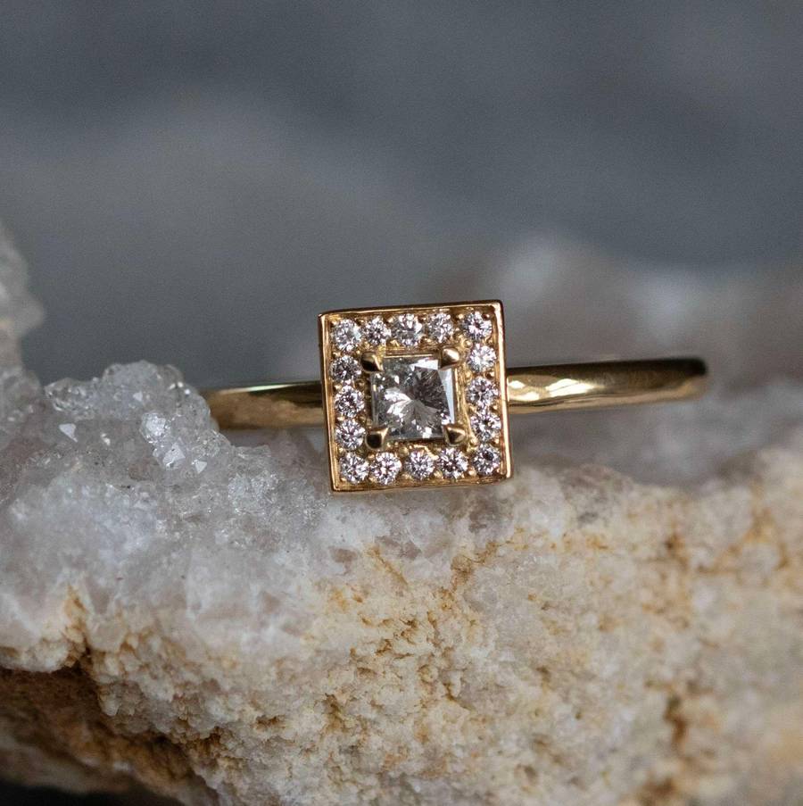 Close-up of bespoke gold engagement ring with square diamond halo set on a textured crystal surface