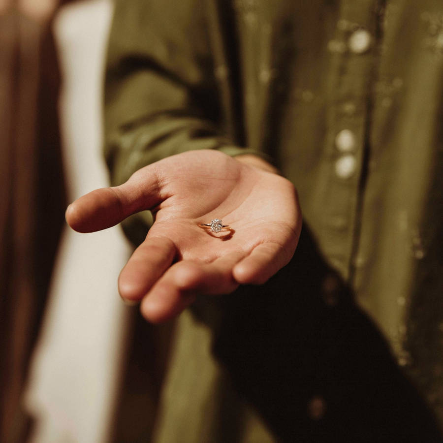 Close-up of a solitaire diamond engagement ring resting in an open hand, captured in warm, intimate lighting.