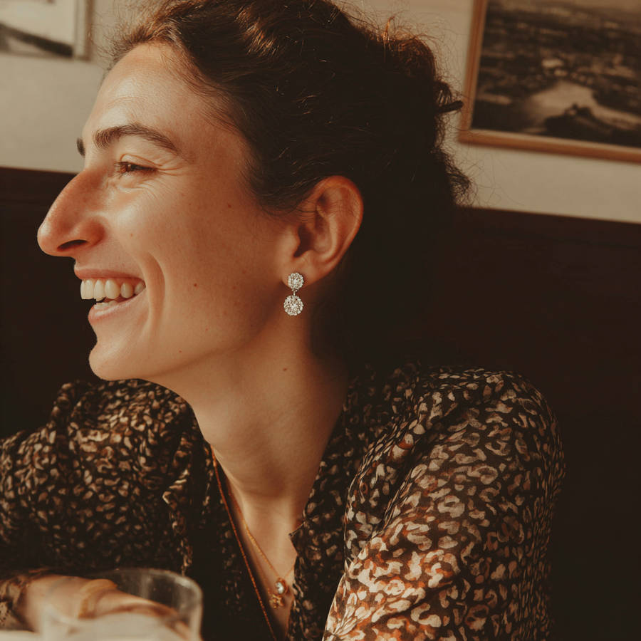 Woman smiling in profile wearing understated bespoke diamond drop earrings in a warm, softly lit setting