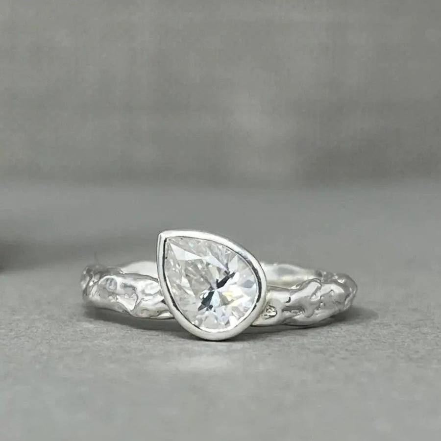 Custom pear-shaped Moissanite bezel engagement ring with an organic textured band on a grey background