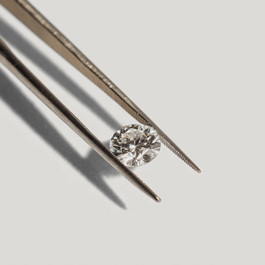 Round brilliant-cut diamond held in tweezers against a clean white background, showcasing sparkle and facets.
