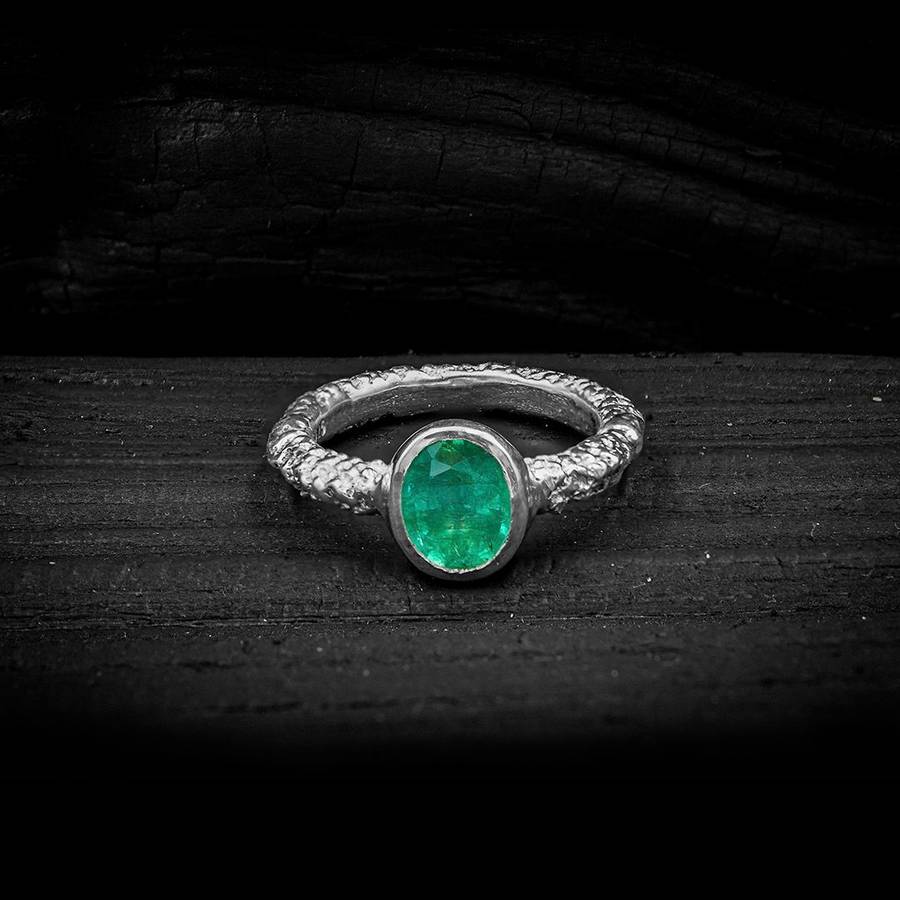 Textured silver ring with an oval green emerald in a bezel setting resting on a dark charcoal surface