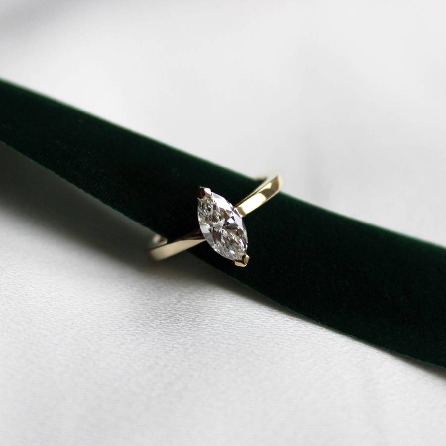 Yellow gold ring with a marquise-cut diamond solitaire set horizontally, displayed on a dark green velvet ribbon.