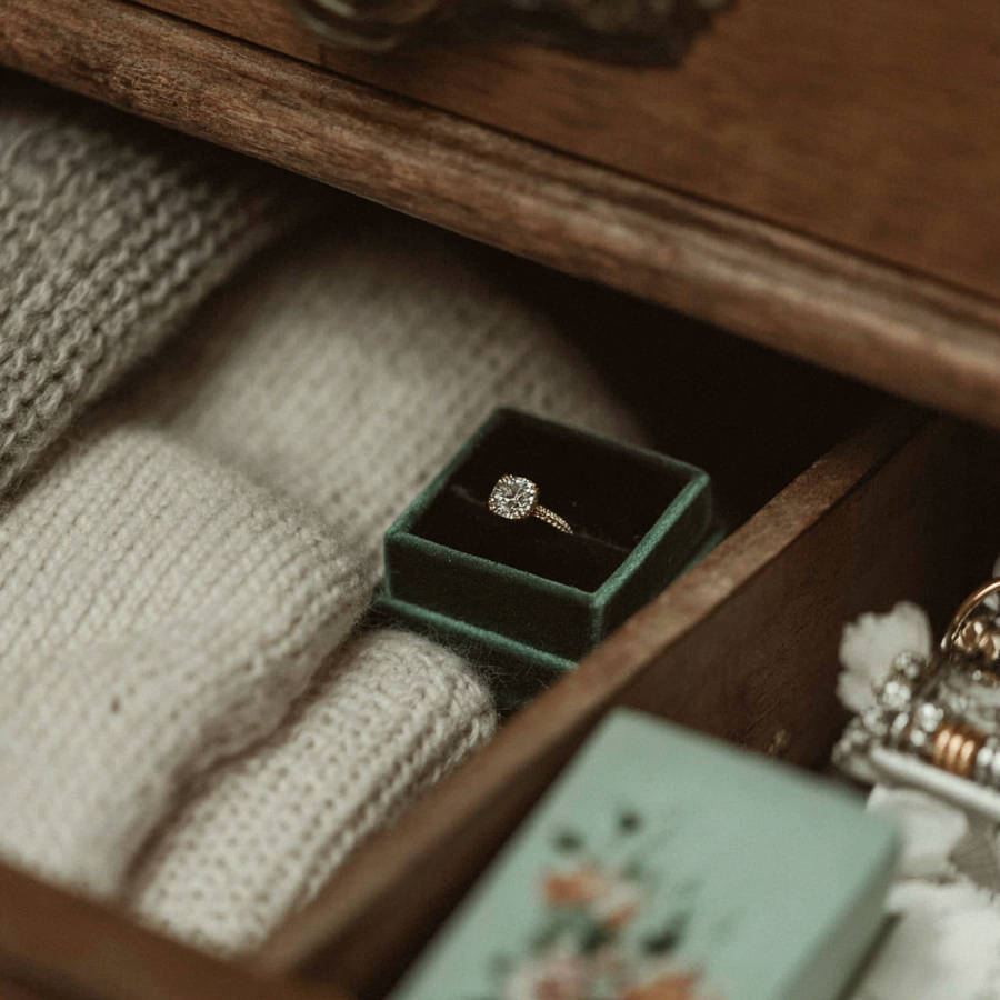 Hidden bespoke engagement ring in a velvet box tucked inside a drawer among folded knitwear and personal belongings.