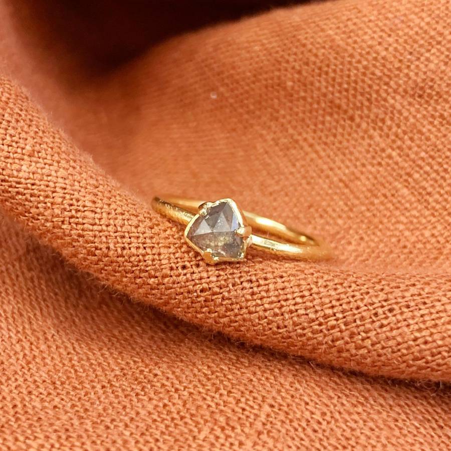 Delicate yellow gold ring with a small geometric grey diamond held by prongs, resting on softly folded terracotta-coloured fabric.