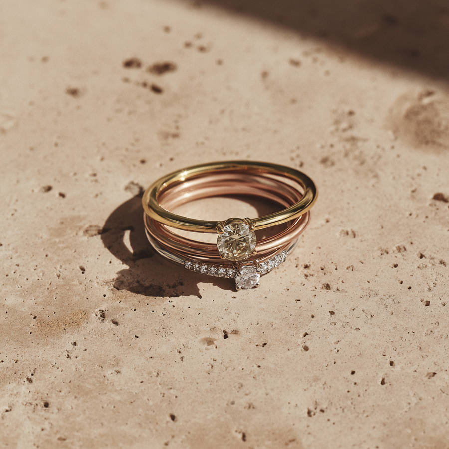 Stacked bespoke engagement rings in yellow and rose gold with diamond accents on a textured stone surface.