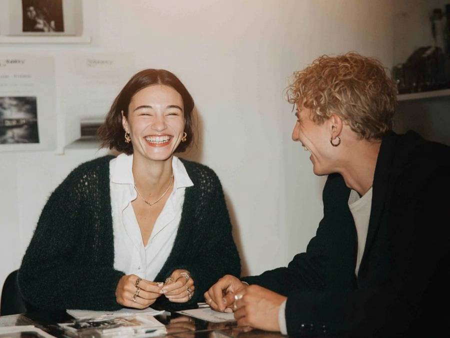 Two people laughing during a jewelry consultation at a table, holding rings and notes in a bright studio setting