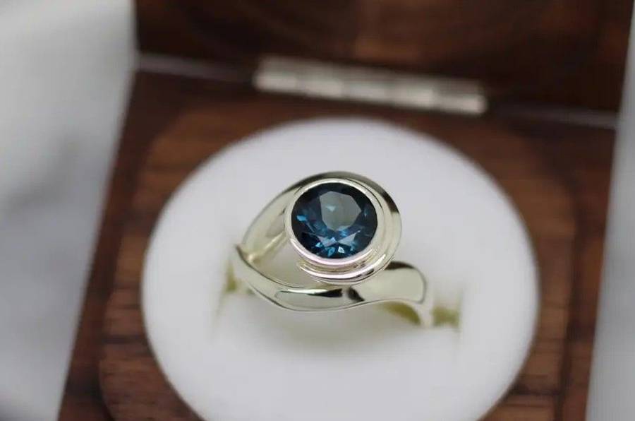 Custom silver ring with a deep blue bezel-set gemstone displayed in an open wooden ring box