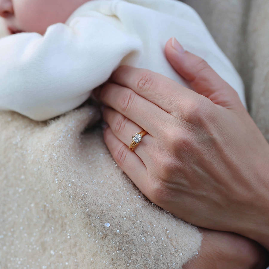 Close-up of a woman holding a baby, wearing a bespoke yellow gold diamond engagement ring on her hand.