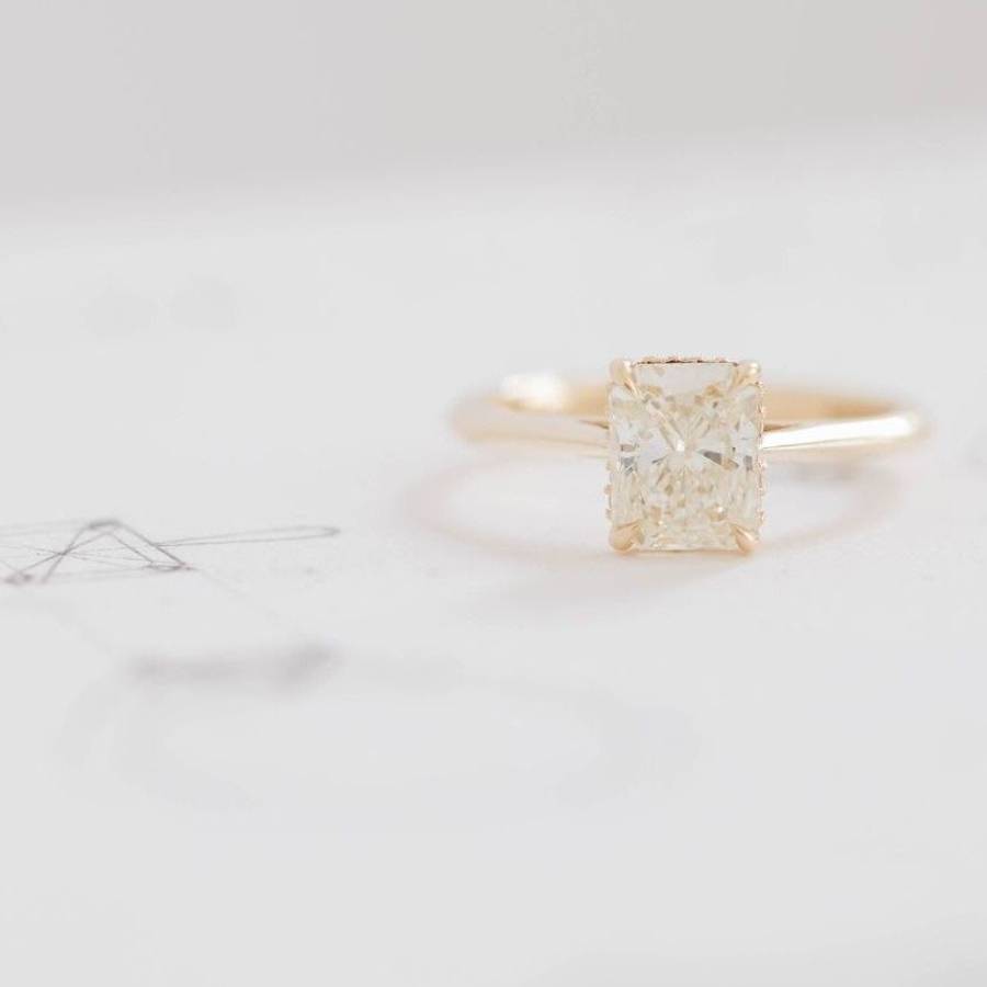 Yellow gold solitaire ring with a radiant-cut pale yellow diamond, displayed on a soft white background.