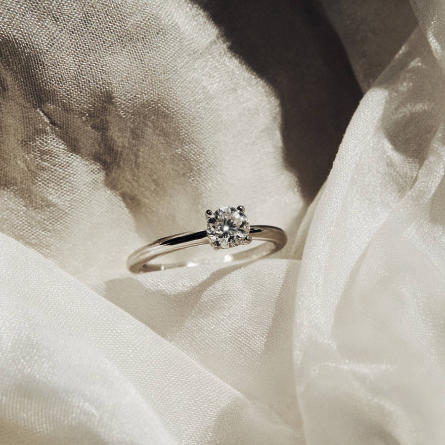 Custom solitaire diamond engagement ring on soft fabric with delicate band and round brilliant stone