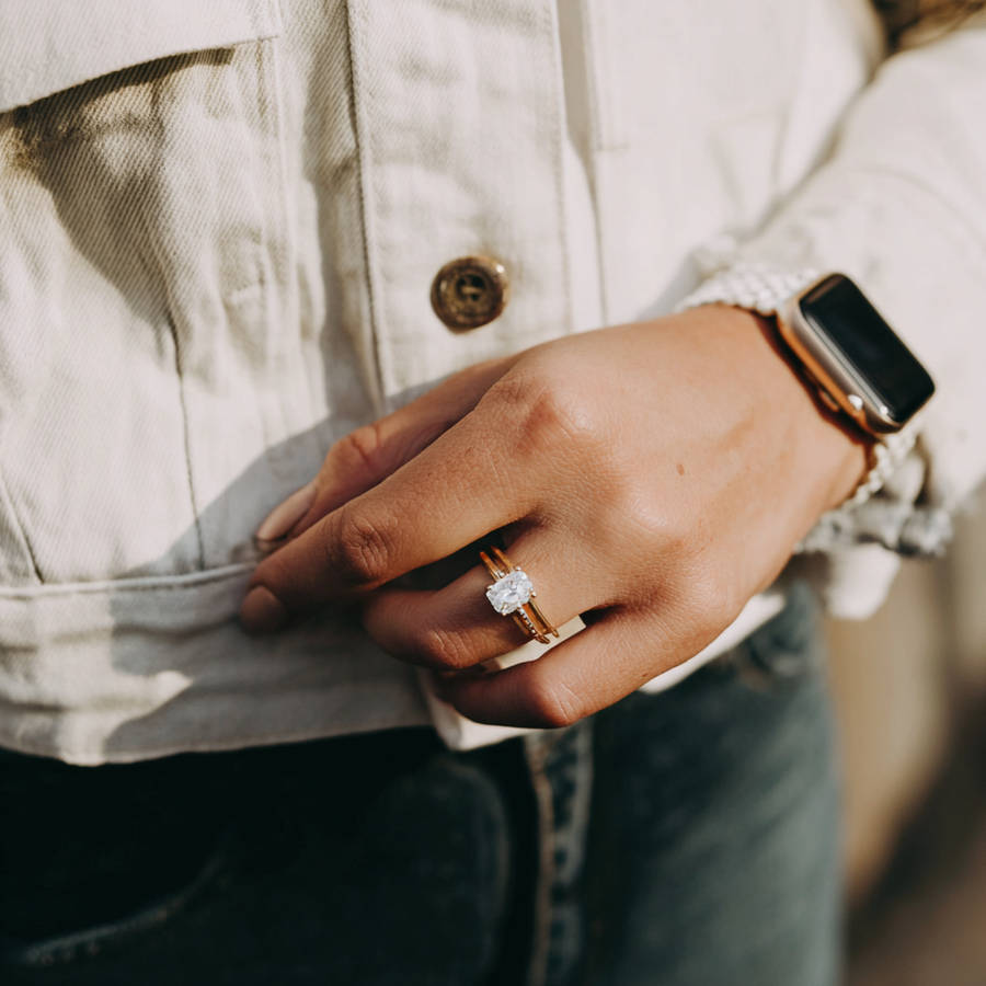 Close-up of hand in casual outfit wearing a bespoke diamond engagement ring and silver smartwatch in natural light
