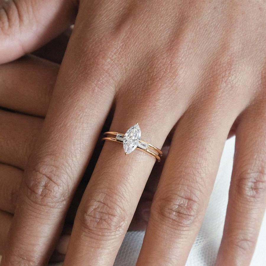 Hand wearing a slim gold ring with a marquise-cut diamond center stone and baguette side diamonds on a double-band setting