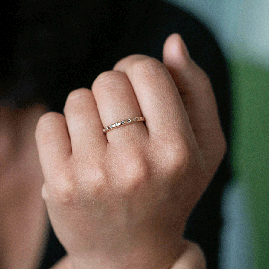 Close-up of a child’s hand wearing a delicate bespoke gold band with tiny diamonds, softly lit against a blurred natural background