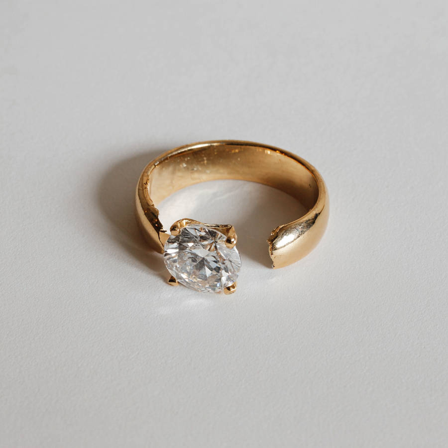 Broken custom gold engagement ring with round diamond, damaged band split open on a neutral background