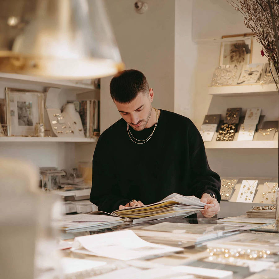 Independent jeweller reviewing diamond paperwork at a studio counter, surrounded by bespoke jewellery displays
