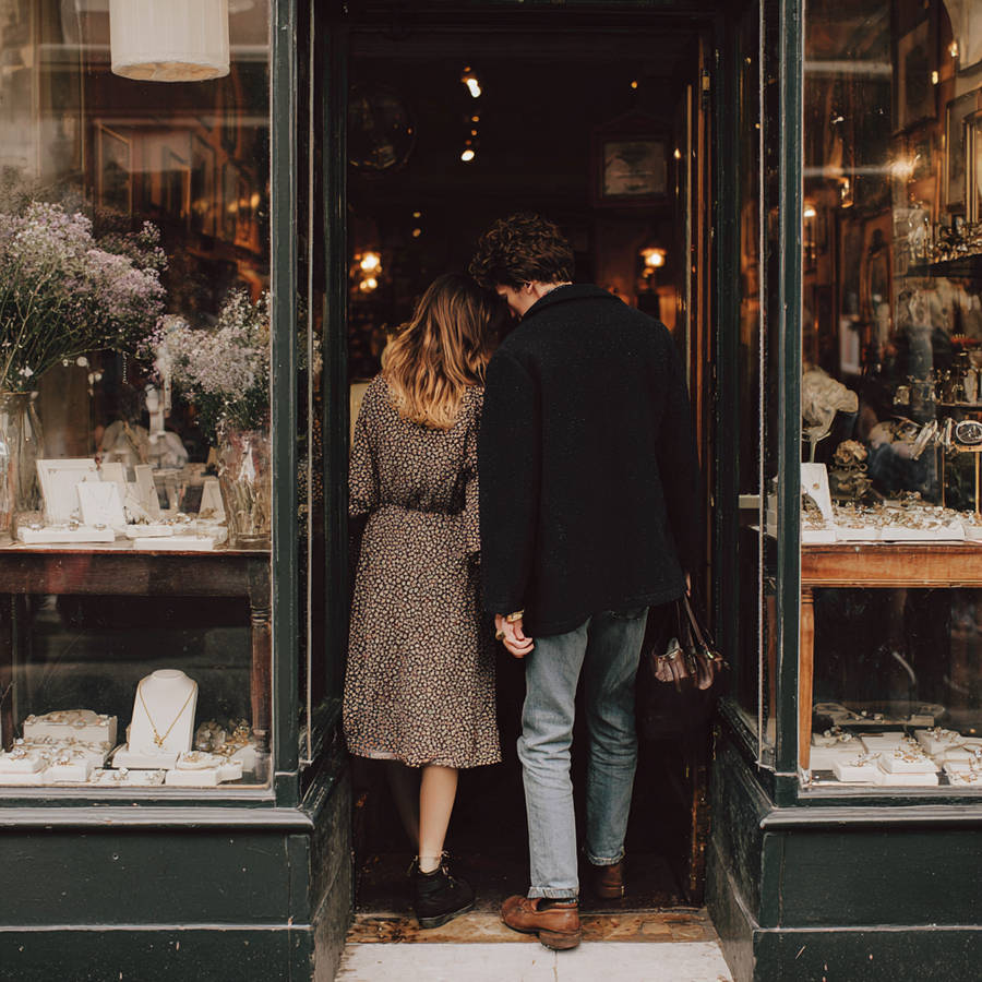 Couple holding hands entering a jewellery shop with window displays of engagement rings and fine jewellery