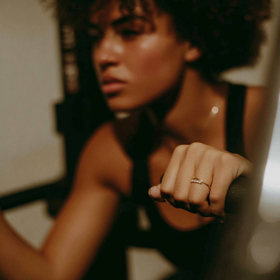 Woman gripping exercise bike handle during workout, wearing a delicate custom ring that catches warm ambient light