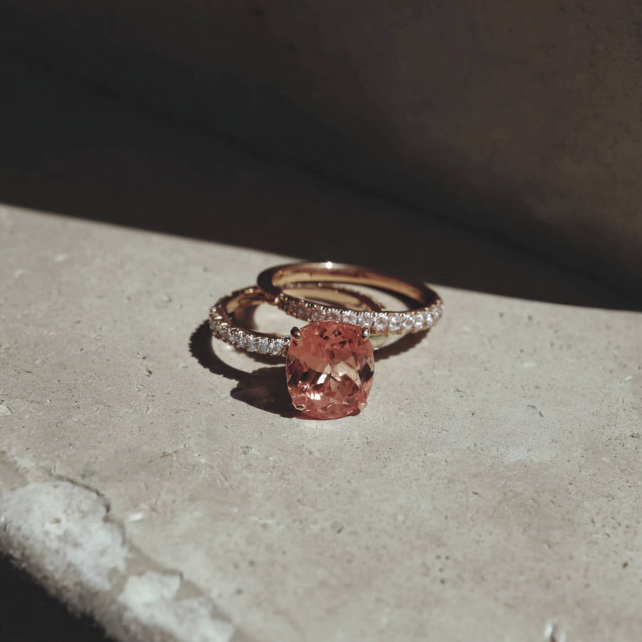 Custom rose gold engagement ring with oval pink gemstone and diamond pavé band resting on a sunlit stone surface