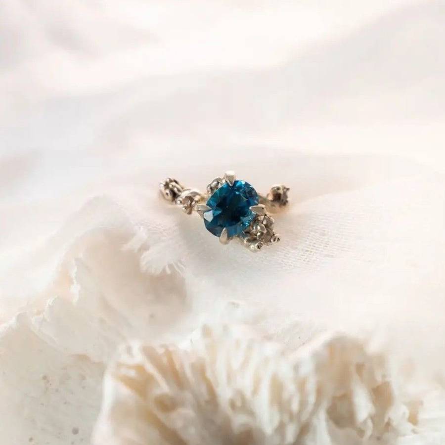 Custom 9ct white gold ring with blue topaz and diamond accents, photographed on soft white fabric background