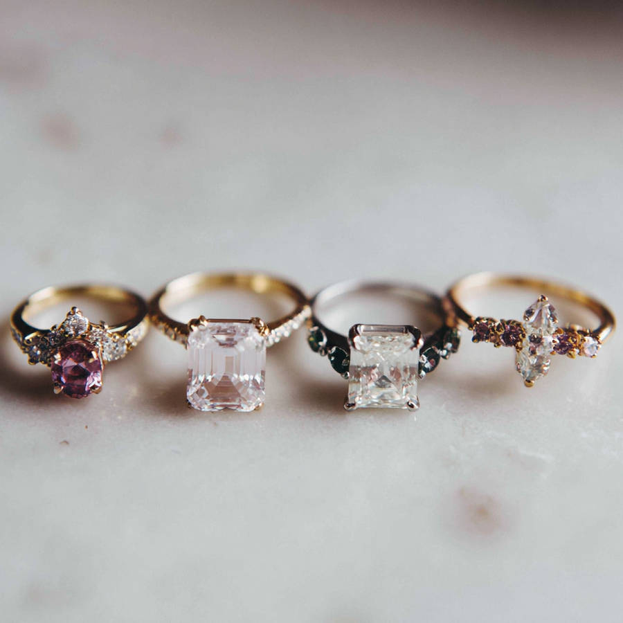 Four bespoke engagement rings with different gemstone cuts and settings lined up on a neutral surface