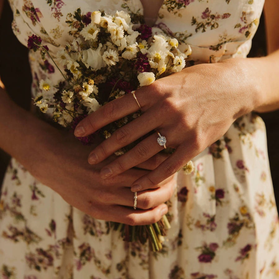 Close-up of woman holding wildflower bouquet, wearing a bespoke diamond engagement ring and delicate bands in warm sunlight
