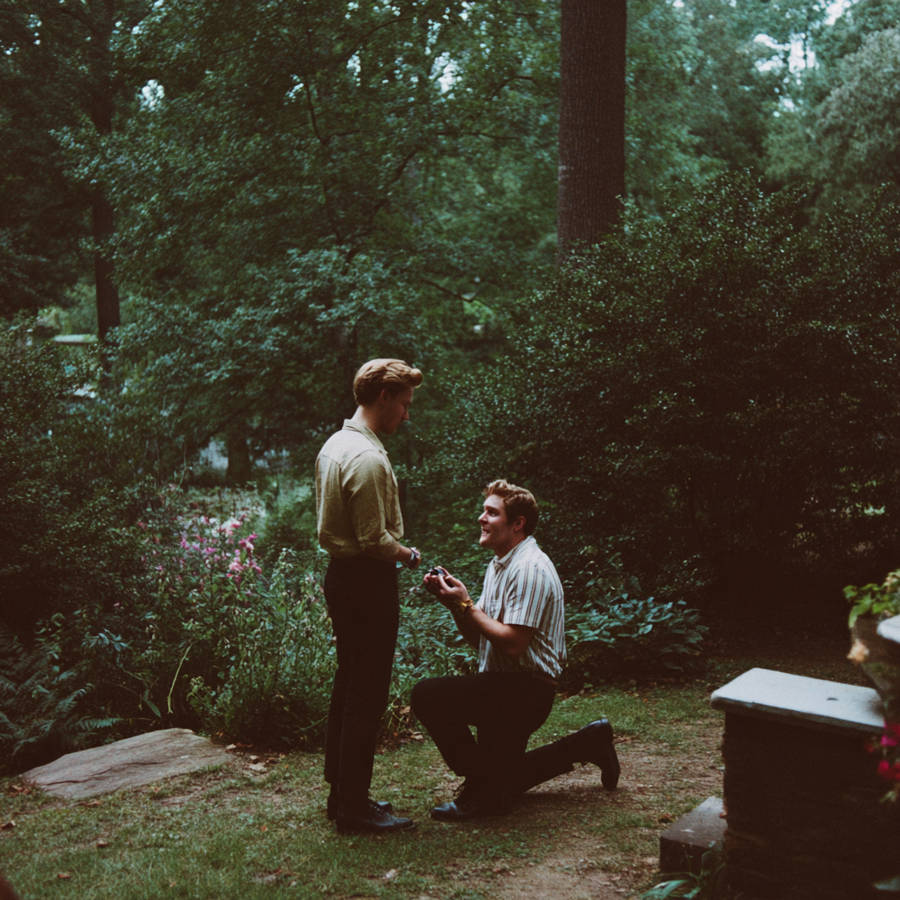 Man kneeling to propose with a bespoke engagement ring to his partner in a lush garden setting