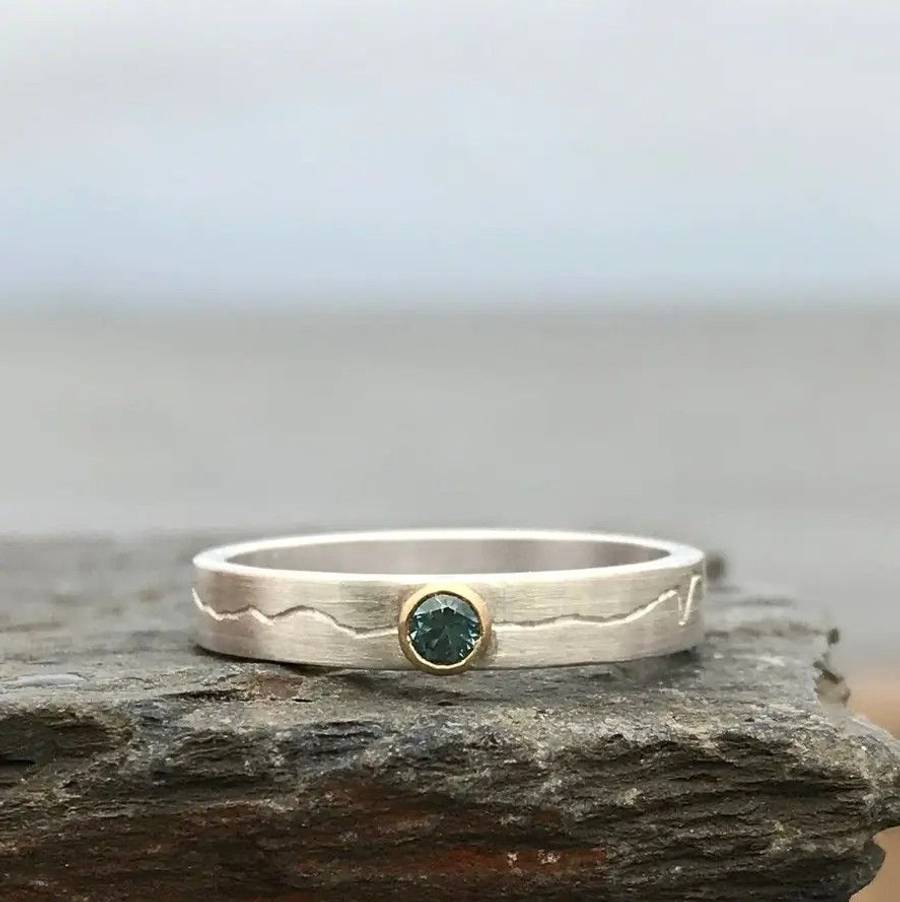 Custom textured silver ring with a dark green gemstone bezel set on a rustic stone surface