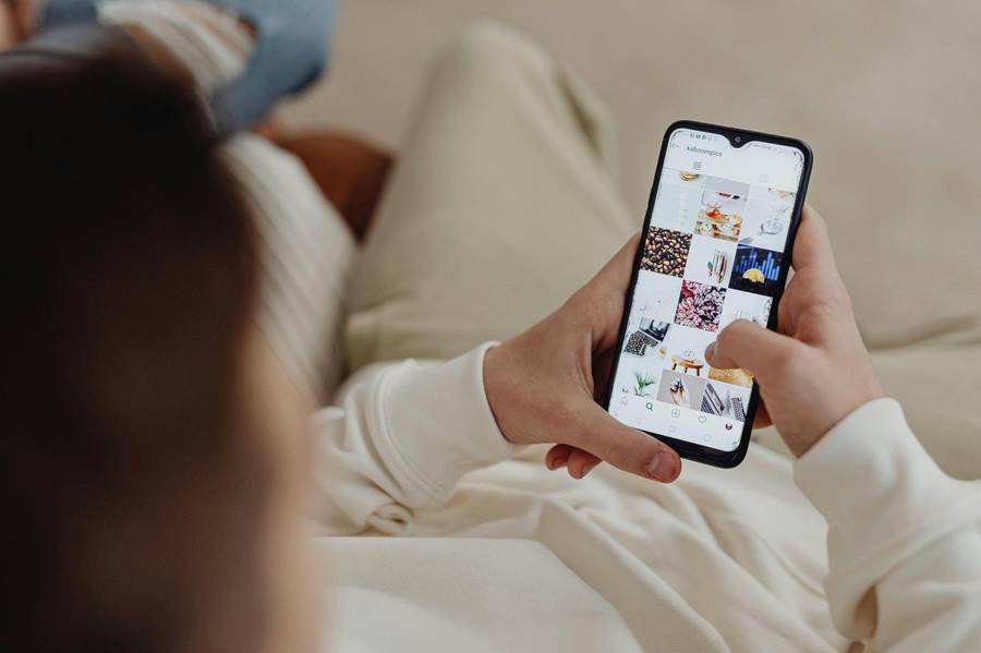 Person lounging and scrolling an Instagram photo grid on a smartphone, browsing visual inspiration.
