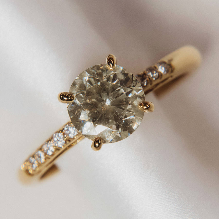 Macro view of a bespoke round diamond engagement ring with pavé band and six-claw yellow gold setting.