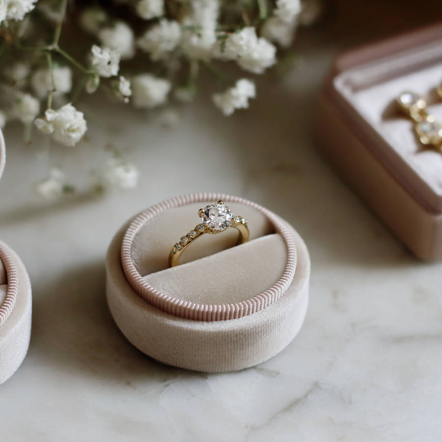 Close-up of a custom diamond engagement ring in a velvet ring box with soft flowers in the background.