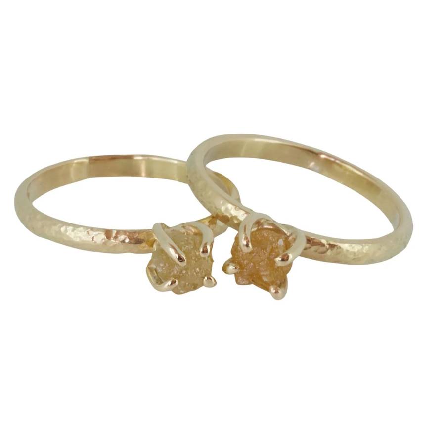 Two minimalist yellow gold rings with hammered bands, each set with a small rough yellow diamond in a prong setting, displayed on a white background.