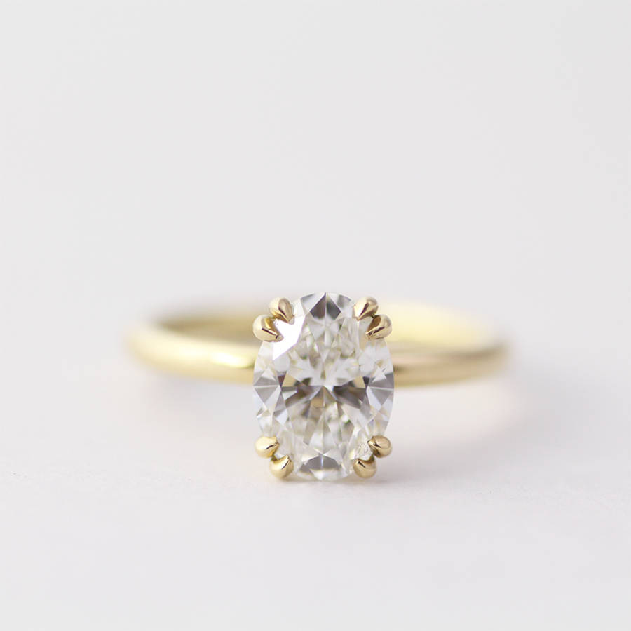 Yellow gold solitaire ring with an oval-cut diamond held in a six-prong setting against a soft neutral background.