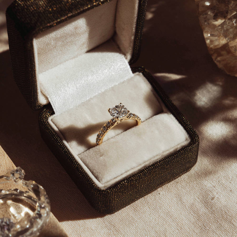 Custom solitaire diamond engagement ring in an open velvet ring box, lit by warm sunlight with soft shadows.