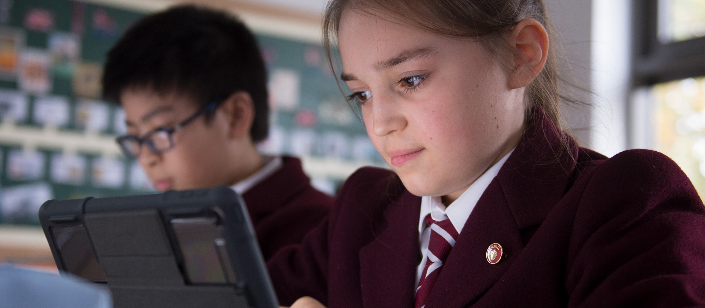 Girl and boy looking at screens in a classroom