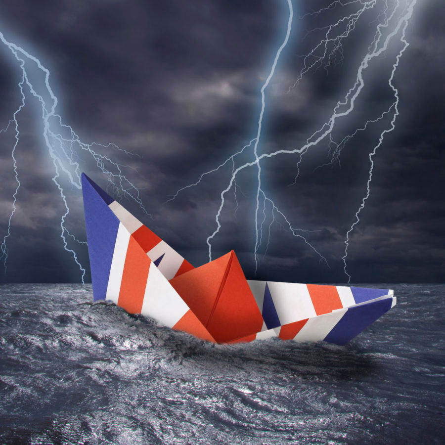 UK paper boat made as the flag of the United Kingdom almost capsizes in high waves. Bolt of lightning i stormy dark sea weather during a thunder-storm with dramatic cloudscape.